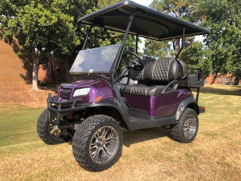 A purple custom 2020 Club Car® Onward™ Lifted 4 Passenger golf cart parked in front of a set of trees. 